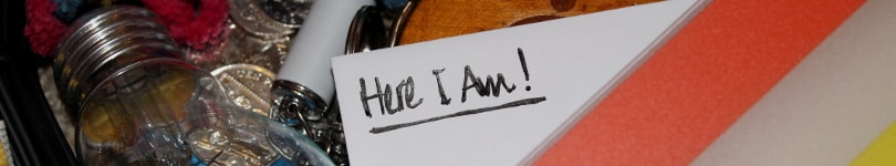 The words 'Here I am!' written on a piece of paper amongst some colourful clutter